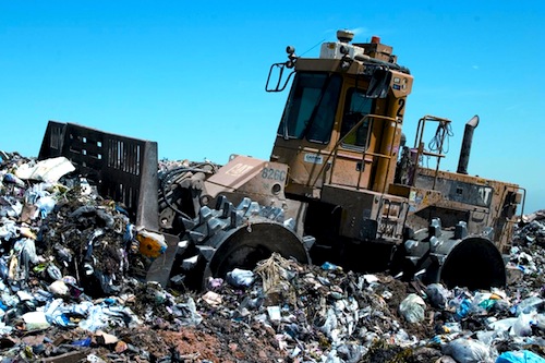 A landfill compactor working a lift face. The steel wheels and cleats are the actual compaction tool, not the blade.